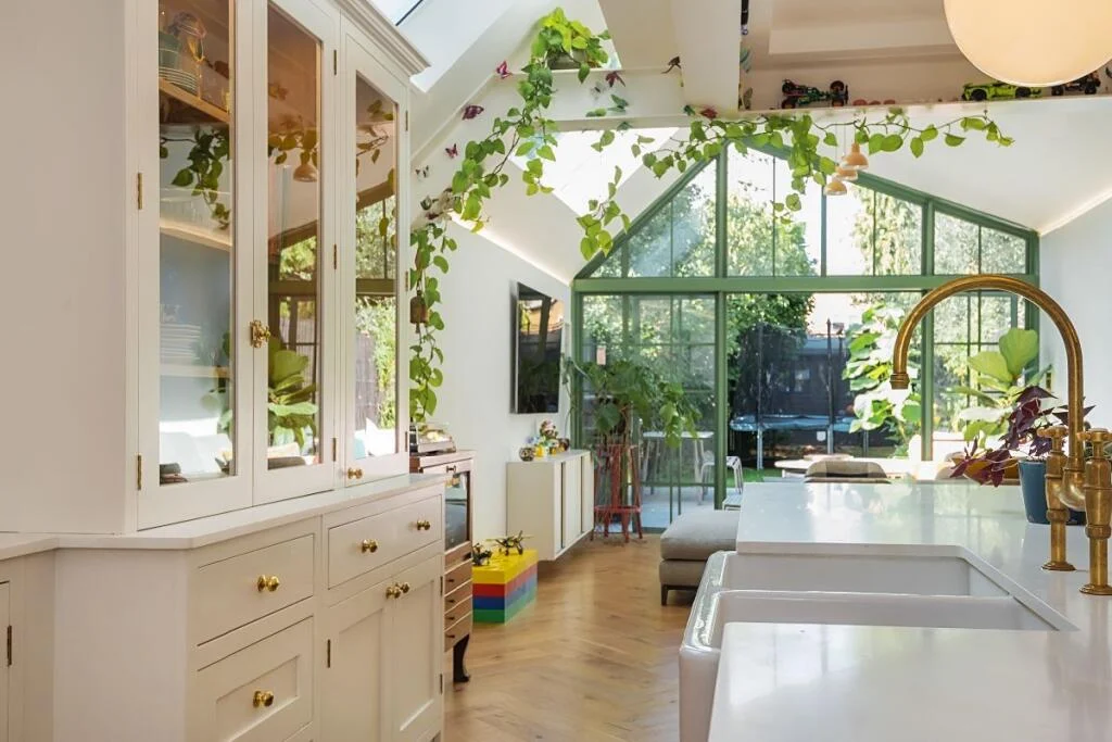 kitchen extension with white cabinetry, trailing plants and green glazed garden doors — Twickenham TW1