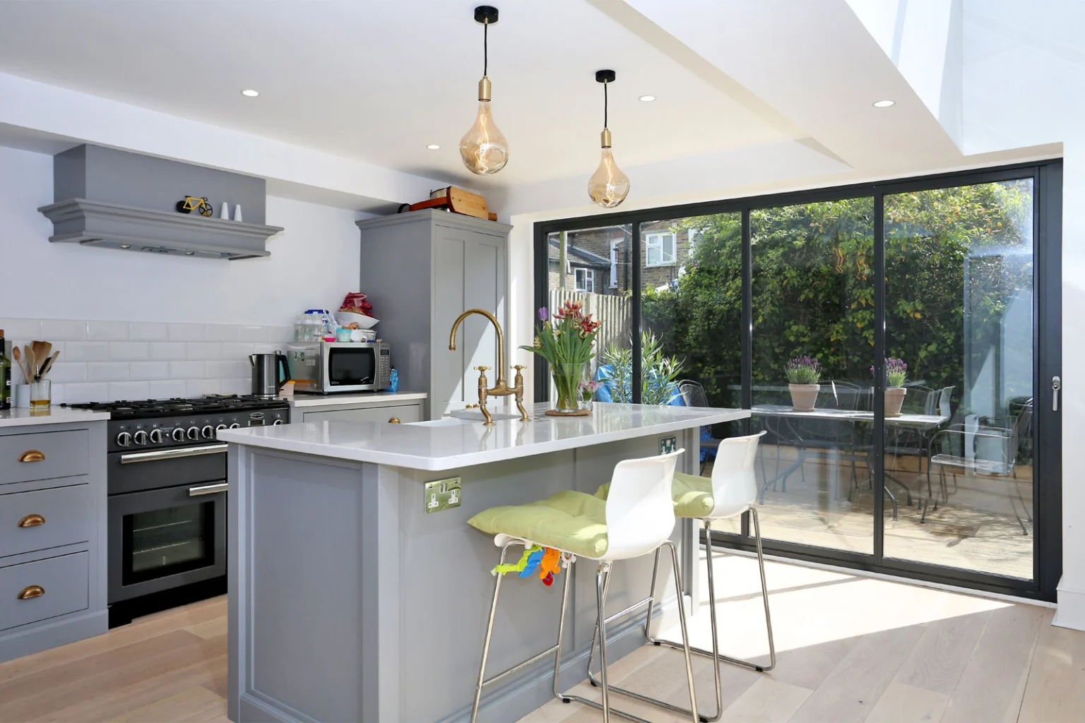 Kitchen island beside black-framed folding garden doors — Hammersmith W6