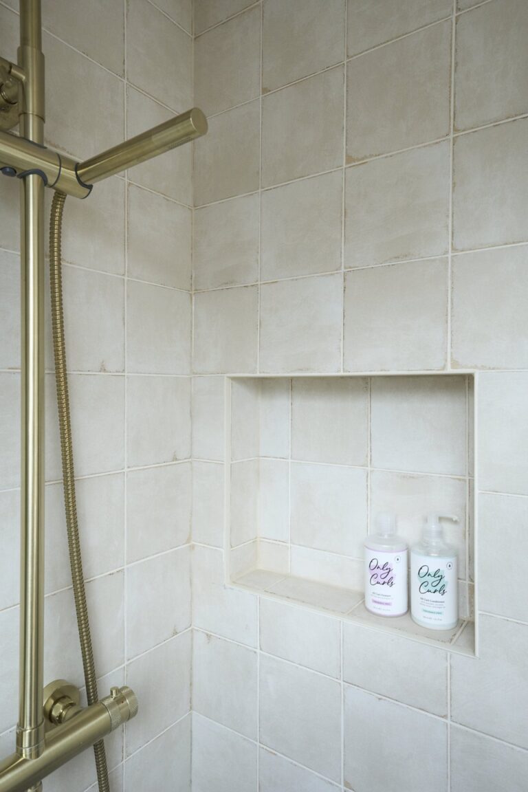 Shower with gold fixtures and hair products on shelf — Chiswick W4