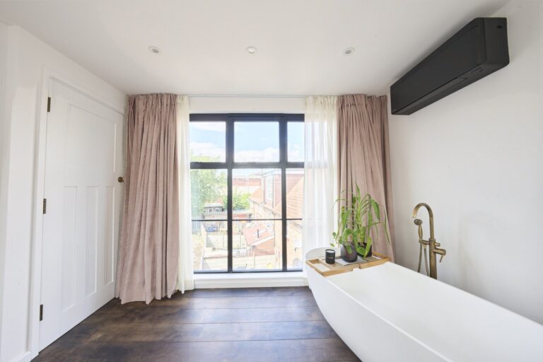 Freestanding bath beside a black-framed window within the loft bedroom — Chiswick W4