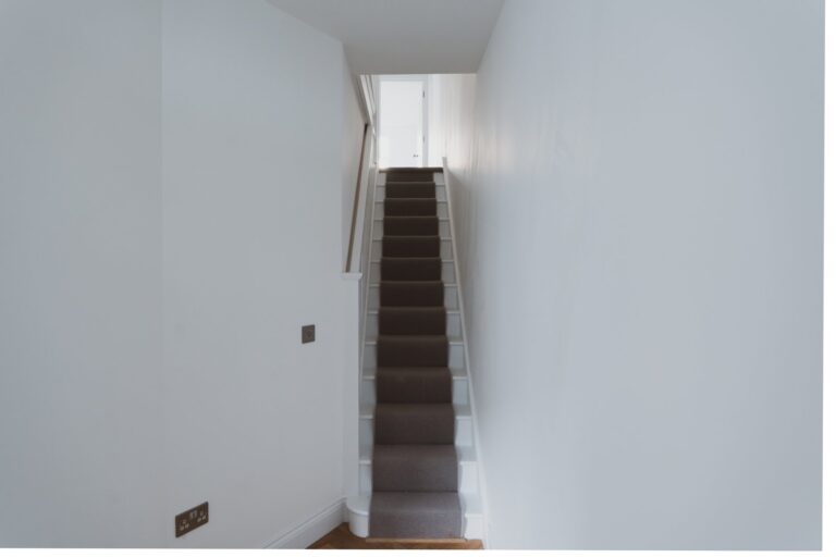Narrow carpeted staircase in empty white hallway — Fulham SW6