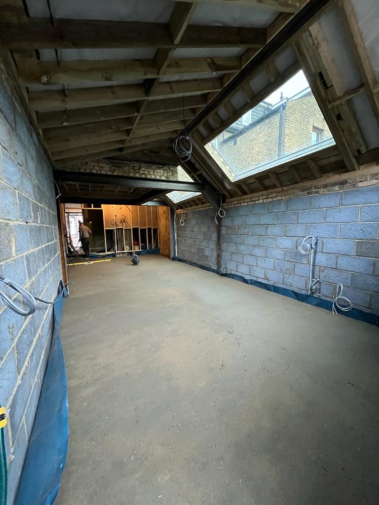 Ash Island extension under construction in Twickenham, showing exposed roof timbers, rooflights, blockwork and electrical wiring.